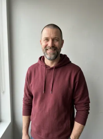 Photo of a bearded man in a maroon hoodie cast as the lead singer